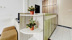 A reception area with a wooden reception desk, two potted plants, a black door, and a wall with vertical stripes and text.