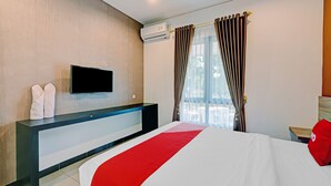 A hotel room with a bed, a TV mounted on the wall, a bedside table, and a window with curtains.