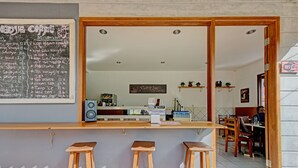 A coffee shop with a chalkboard menu listing various coffee and tea options. There are wooden stools and a counter with a speaker.