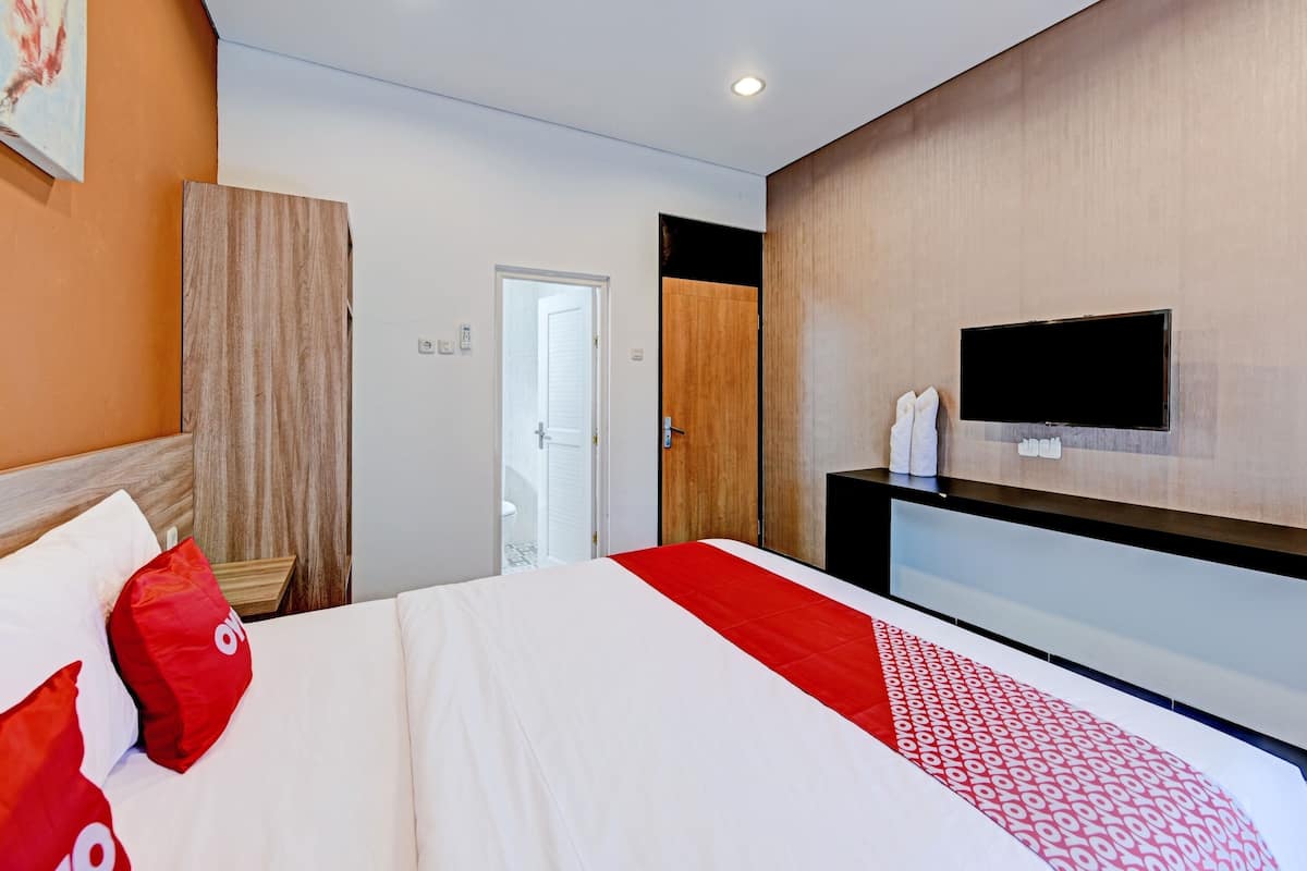 A modern hotel room with a large bed, a TV mounted on the wall, and a wooden wardrobe.