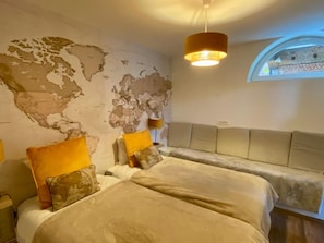 Una habitación con un mapa mundial en la pared, una cama con cabecera, un ventanal y una lámpara colgante.