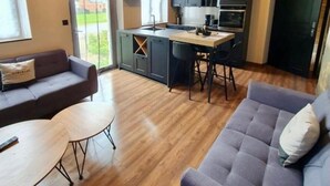 Una cocina moderna con techo de ladrillo, zona de comedor con sofá y mesa, y vista a un paisaje verde a través de ventanales arqueados.