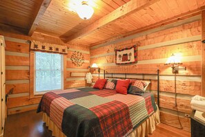 Une chambre à coucher dans une cabane en bois, avec un lit, deux lampes fixées au mur, une fenêtre avec des stores et une couvre-lit matelassé.