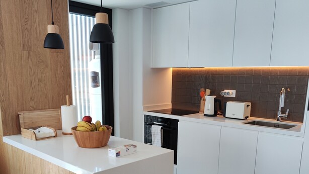 A modern kitchen with white cabinetry, a central island, a built-in oven, and a black countertop.