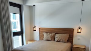 A modern bedroom with a wooden bed, a bench, two bedside tables, and pendant lights.