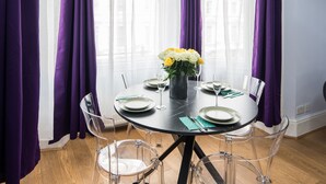 A round dining table with clear chairs, a vase with yellow flowers, and a black tablecloth. - Gloucester Station Gem, 3 Bedroom Oasis (London)