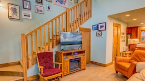 A living room with a wooden staircase, a fireplace, a television, and a red chair.