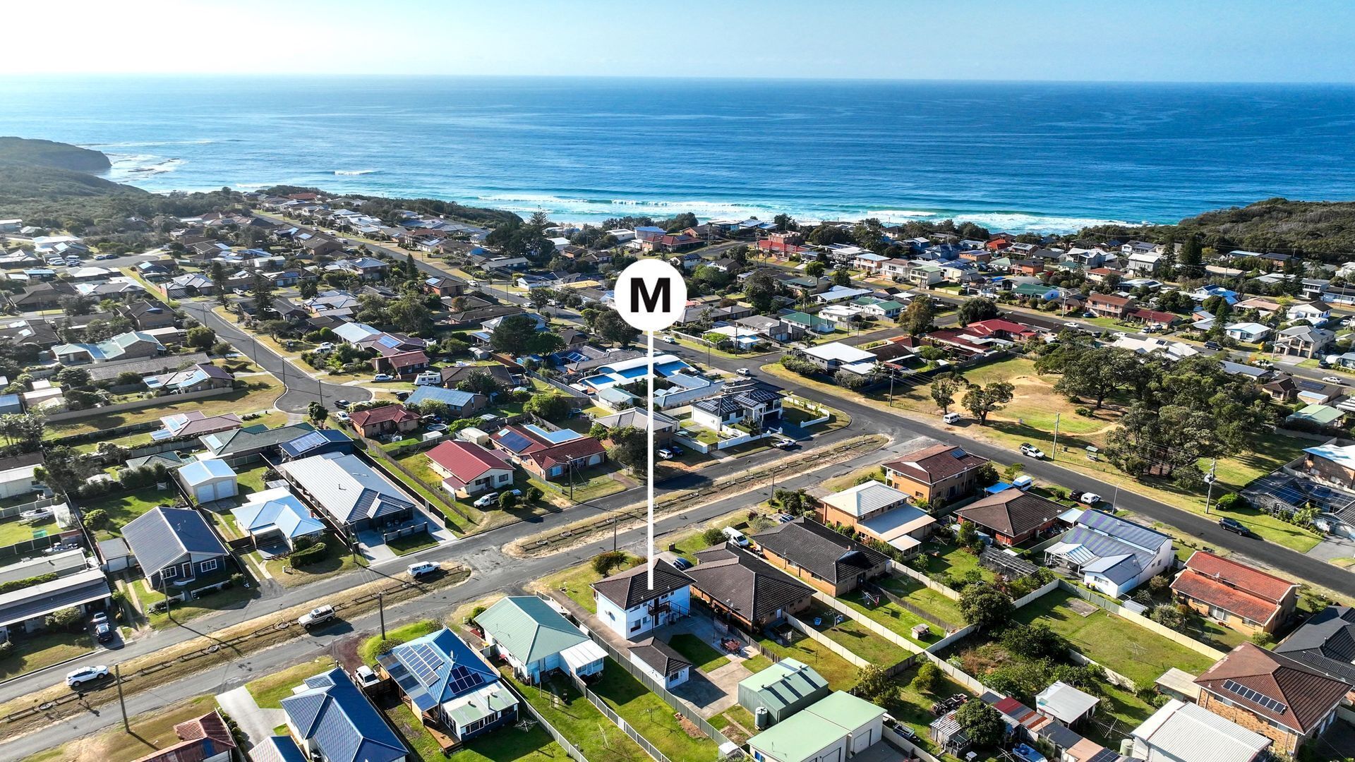 An aerial view of a residential area with houses, roads, and a large body of water in the background.