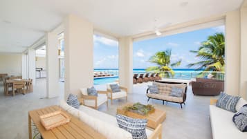 A spacious living area with a view of the ocean, furnished with sofas, chairs, and a wooden table.