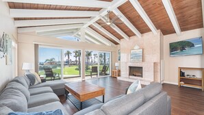 A spacious living room with a high ceiling, a fireplace, and a view of a golf course. - 6BR Oceanfront Retreat, Steps to Beach & Balboa Pier with AC! (Newport Beach)