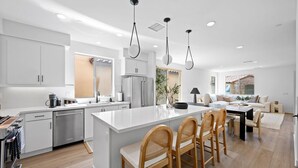 Eine moderne Küche mit weißen Schränken, einer zentralen Kochinsel mit Barhocker und einem Essbereich mit Tisch und Stühlen.