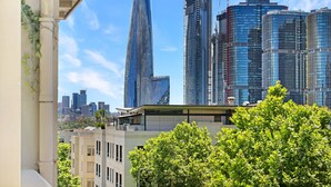 Un paisaje urbano con rascacielos modernos, incluyendo una edificación curva distintiva, y árboles verdes exuberantes en primer plano.