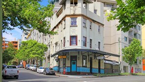 Un edificio en esquina con puerta azul, un balcón y un letrero que indica un hotel.