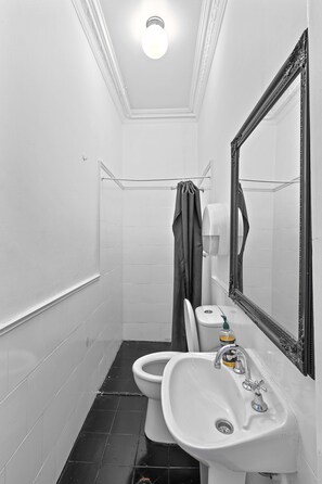 Bathroom features a pedestal sink, toilet, and large mirror with ornate frame, set against white and black tile walls and floor.
