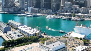 Un paisaje urbano con modernos rascacielos, una marina con barcos y un cielo azul despejado.