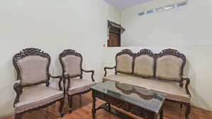 Une pièce comprenant deux fauteuils en bois richement décorés et un canapé assorti, une table basse avec un plateau en verre, et une petite fenêtre dotée d’un volet en bois.