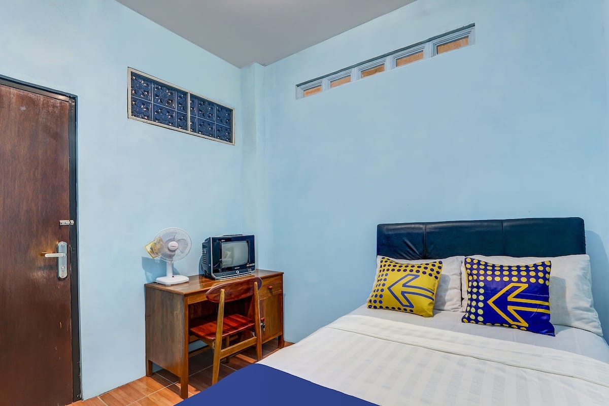 A bedroom with a bed, a wooden nightstand, a television, and a wall-mounted air conditioning unit.