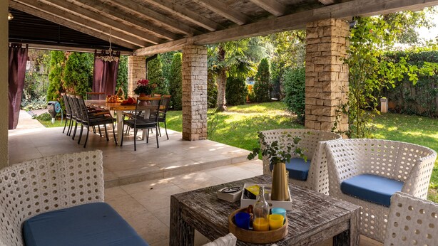 An outdoor patio area with wicker furniture, a stone pillar, and a view of a well-maintained garden. - Villa with pool, up to 12 people,6 bedrooms, close to the beach, garden, parking (Porec)
