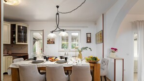 A dining area with a wooden table, four chairs, and a chandelier. There is a kitchen with cabinets and a window in the background. - Villa with pool, up to 12 people,6 bedrooms, close to the beach, garden, parking (Porec)