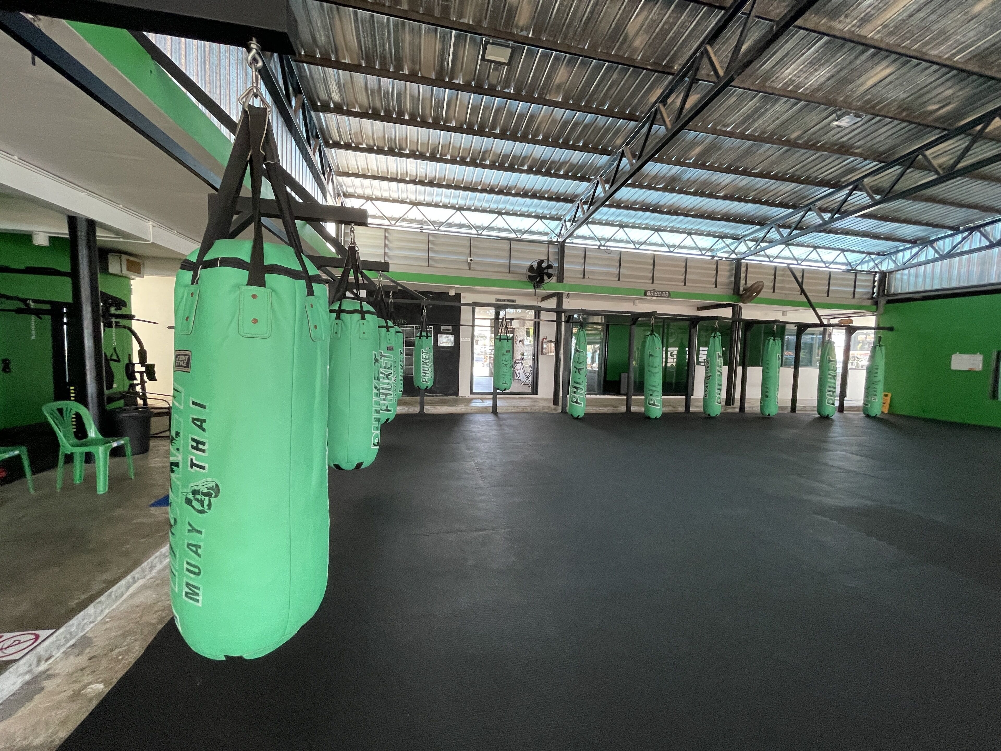 A gym with green walls and a high ceiling, featuring multiple punching bags and exercise equipment.