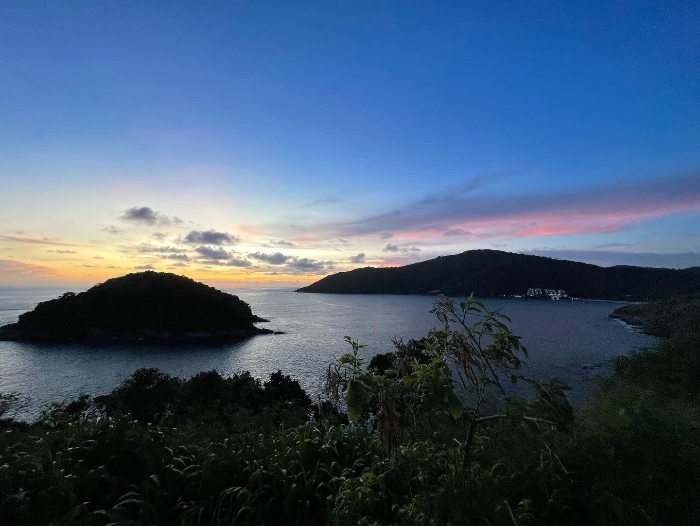 A coastal landscape with a small island and a distant mountain range during sunset.