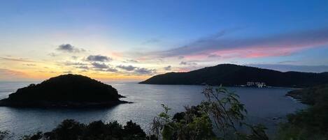 A coastal landscape with a small island and a distant mountain range during sunset.