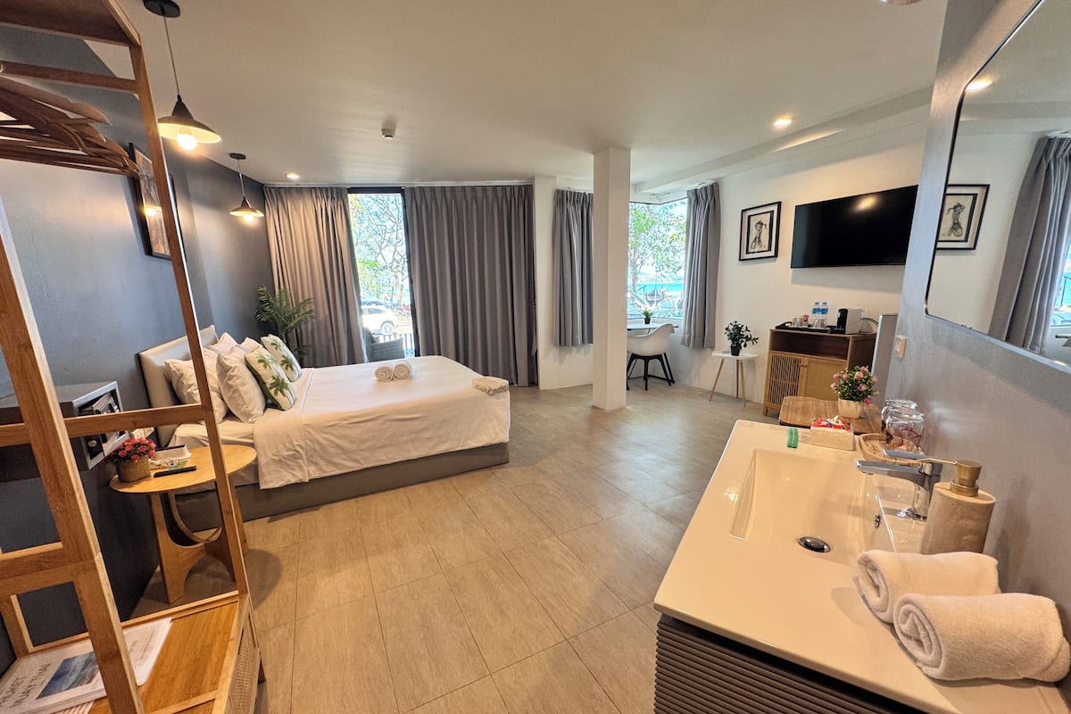 A modern hotel room with a bed, a desk, a bathroom with a sink and mirror, and a TV mounted on the wall.