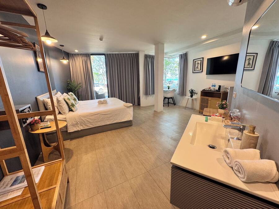 Una habitación de hotel moderna con cama, escritorio, baño con lavamanos y espejo, y un televisor montado en la pared.