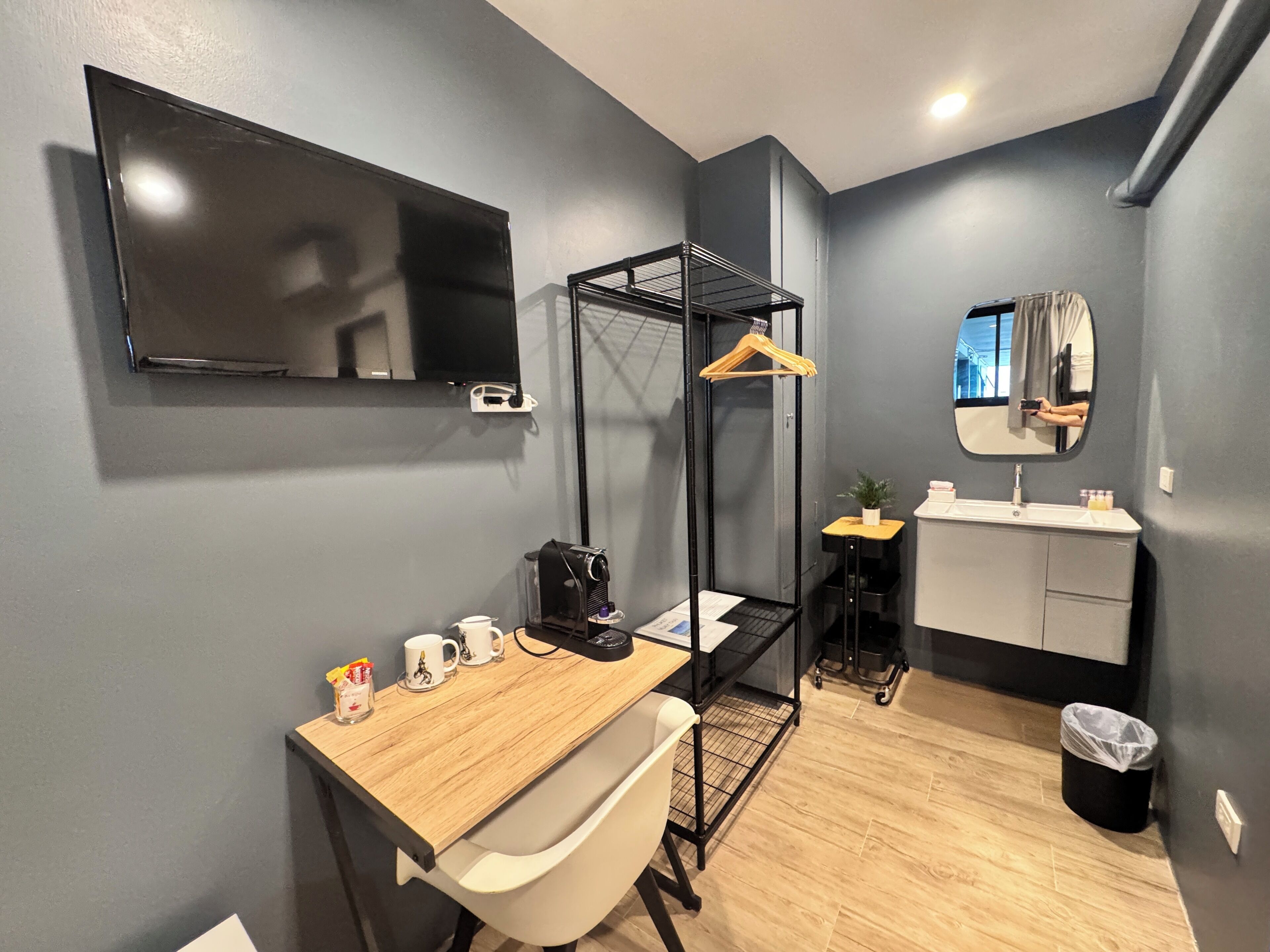 Une chambre d’hôtel compacte, dotée d’un bureau en bois, d’un organiseur suspendu noir, d’une petite plante en pot, d’un miroir et d’un téléviseur fixé au mur.
