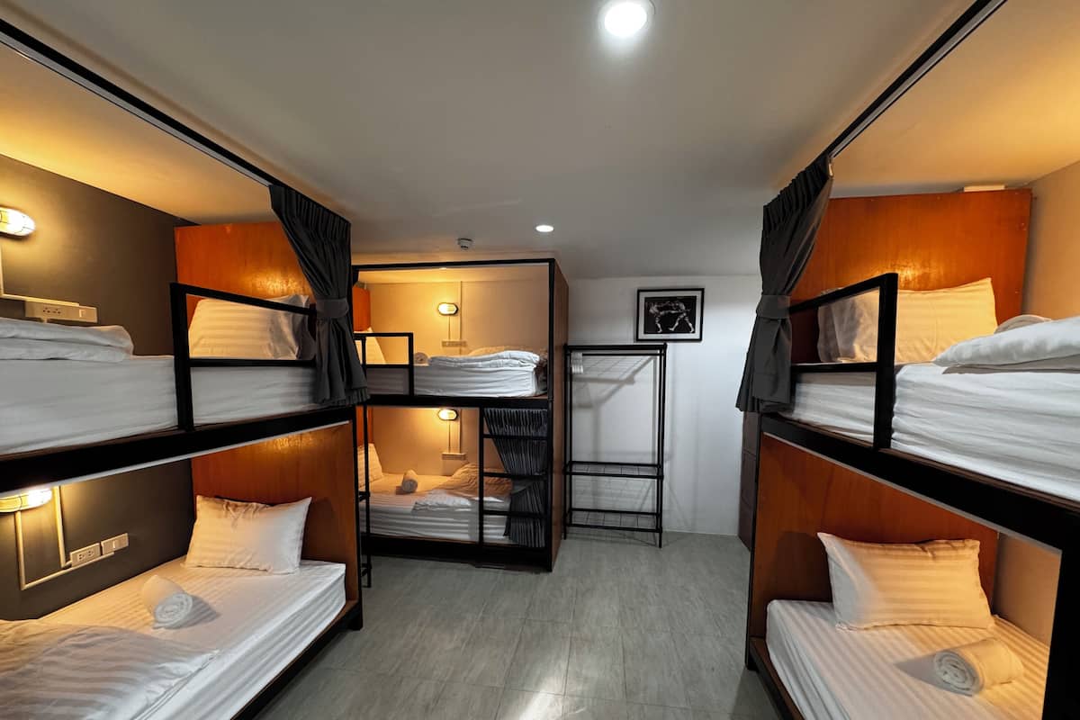 A compact hotel room with bunk beds, a small seating area, and a wall-mounted shelf.