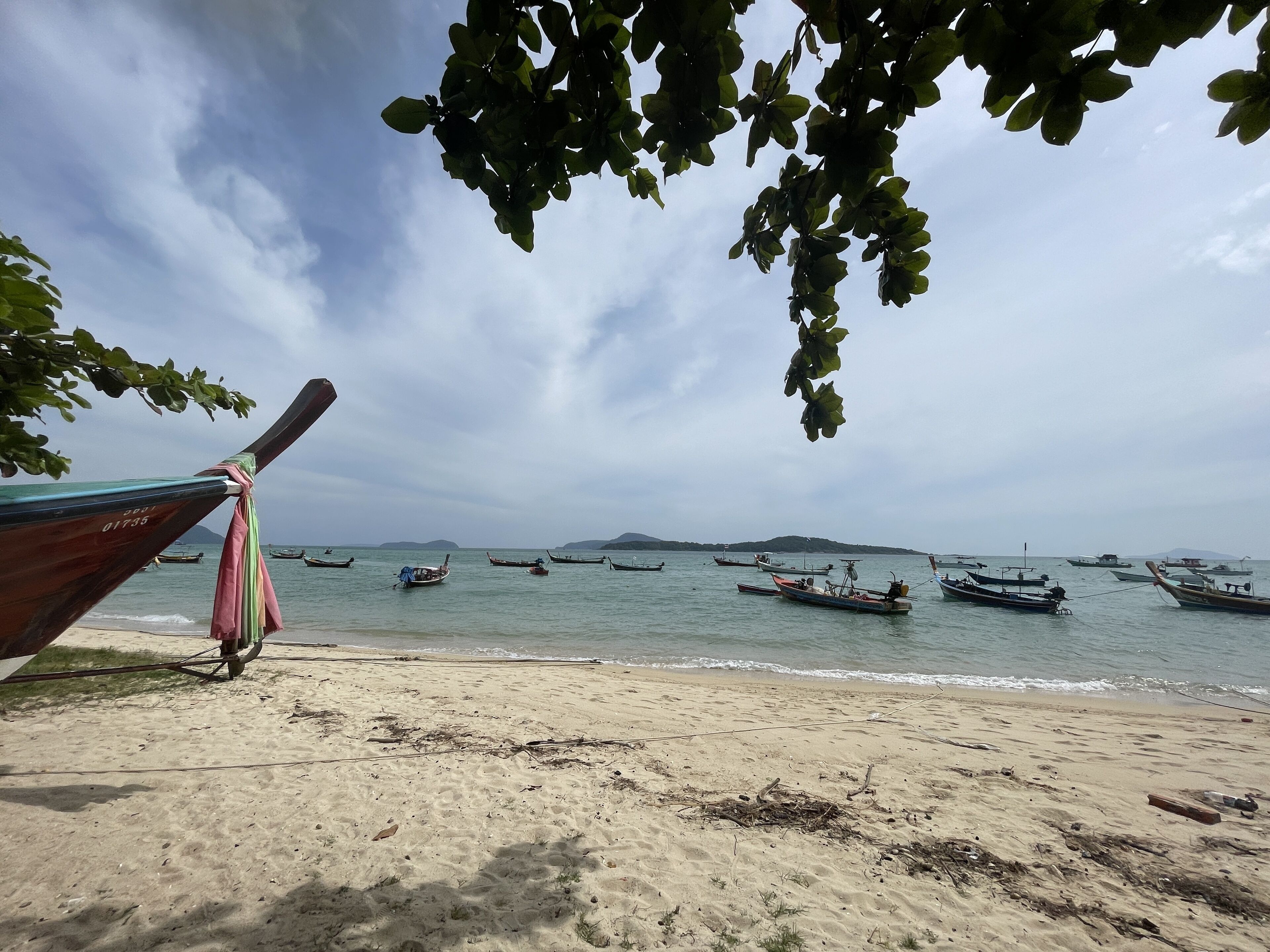 A beach with boats in the water and a boat tied to a tree on the shore.