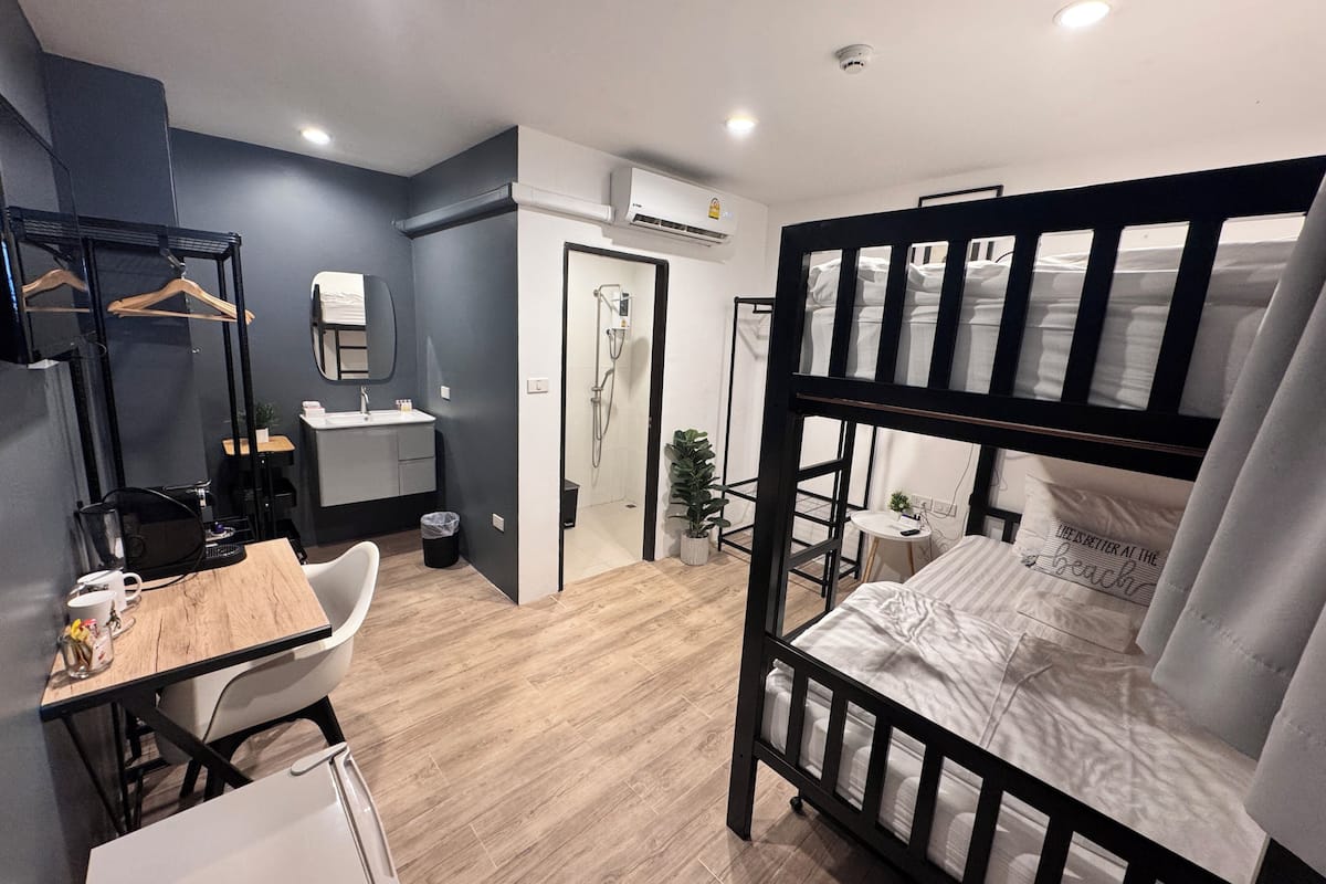 A compact room with a bunk bed, a desk with a chair, a small sink, and a mirror.