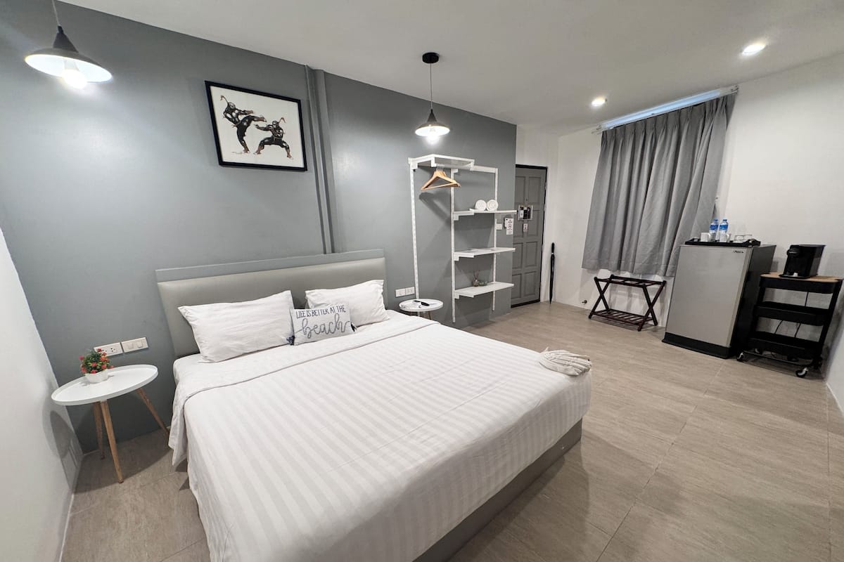 A modern hotel room with a large bed, bedside tables, a wardrobe, a desk with a chair, and a small plant.
