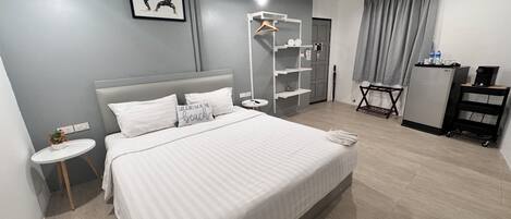 Une chambre d’hôtel moderne, dotée d’un grand lit, de tables de chevet, d’une armoire, d’un bureau avec une chaise et d’une petite plante.