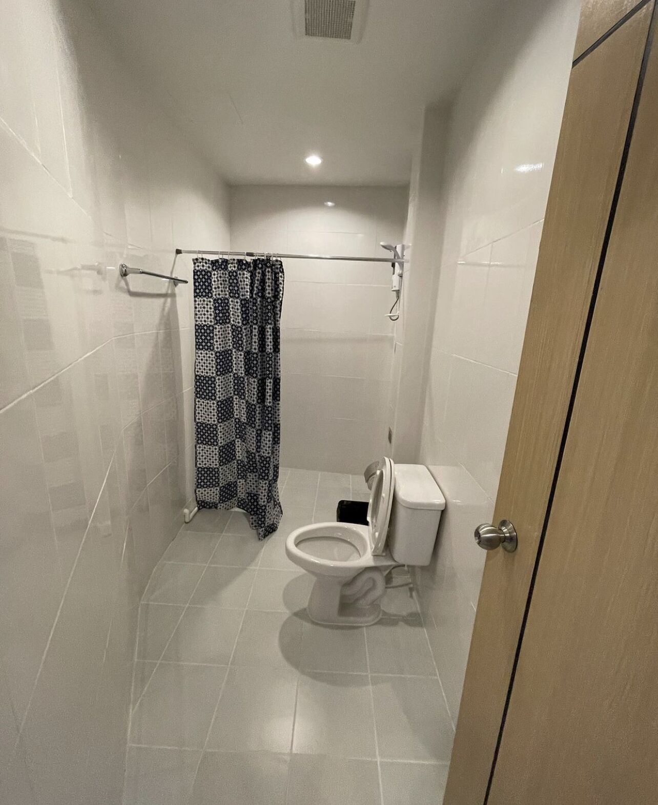 A small, modern bathroom with a toilet, a shower curtain, and tiled walls.