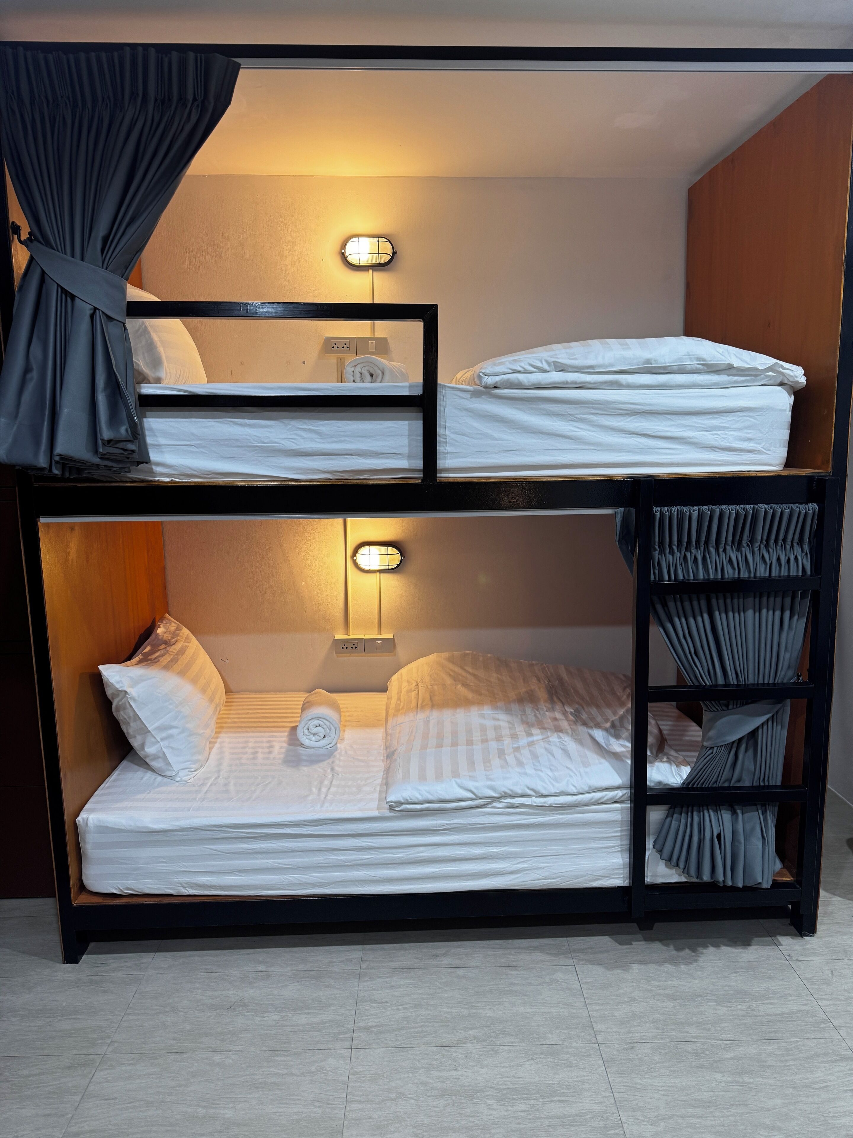 A bunk bed with two levels, each with a pillow and a rolled towel. There are wall-mounted lights above each bed.