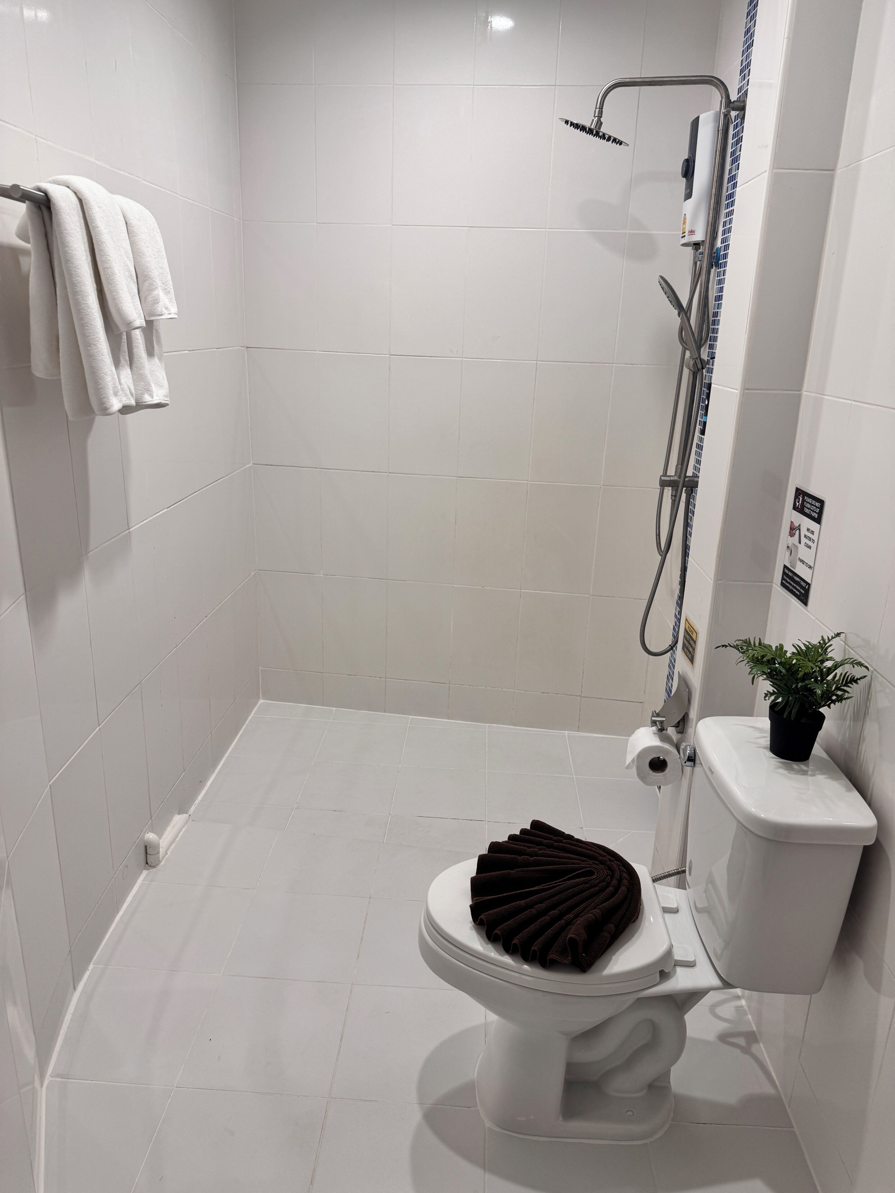 A modern bathroom with white tiles, a shower, a toilet with a towel rack, and a small potted plant.