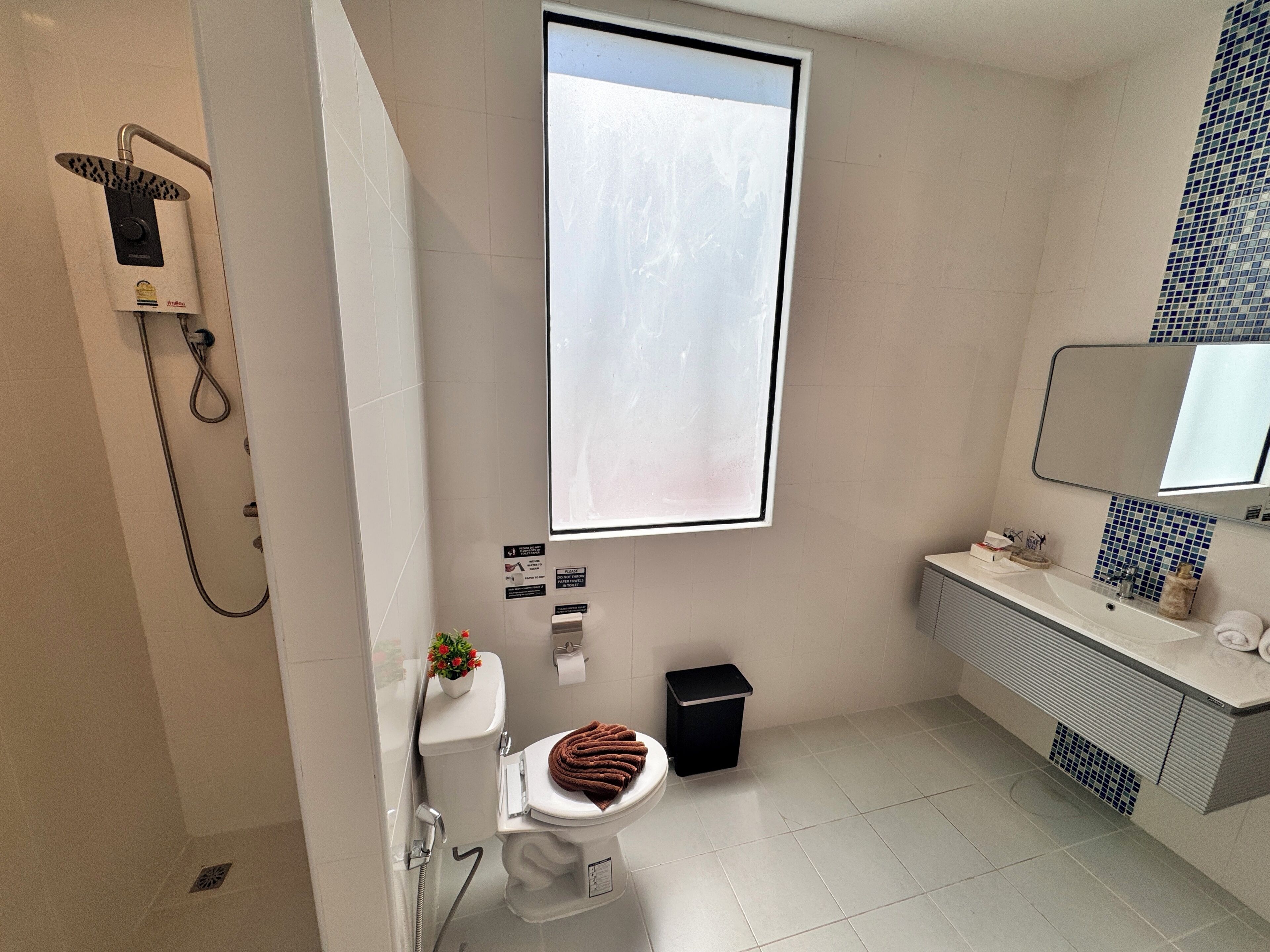 A modern bathroom with a shower, toilet, sink, and a large window.