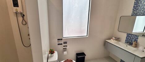 A modern bathroom with a shower, toilet, sink, and a large window.