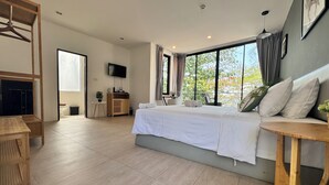 A modern hotel room with a large bed, a TV, a wooden desk, and a balcony with a view. - Phuket Muay Thai Hotel Rawai Beach (Rawai)