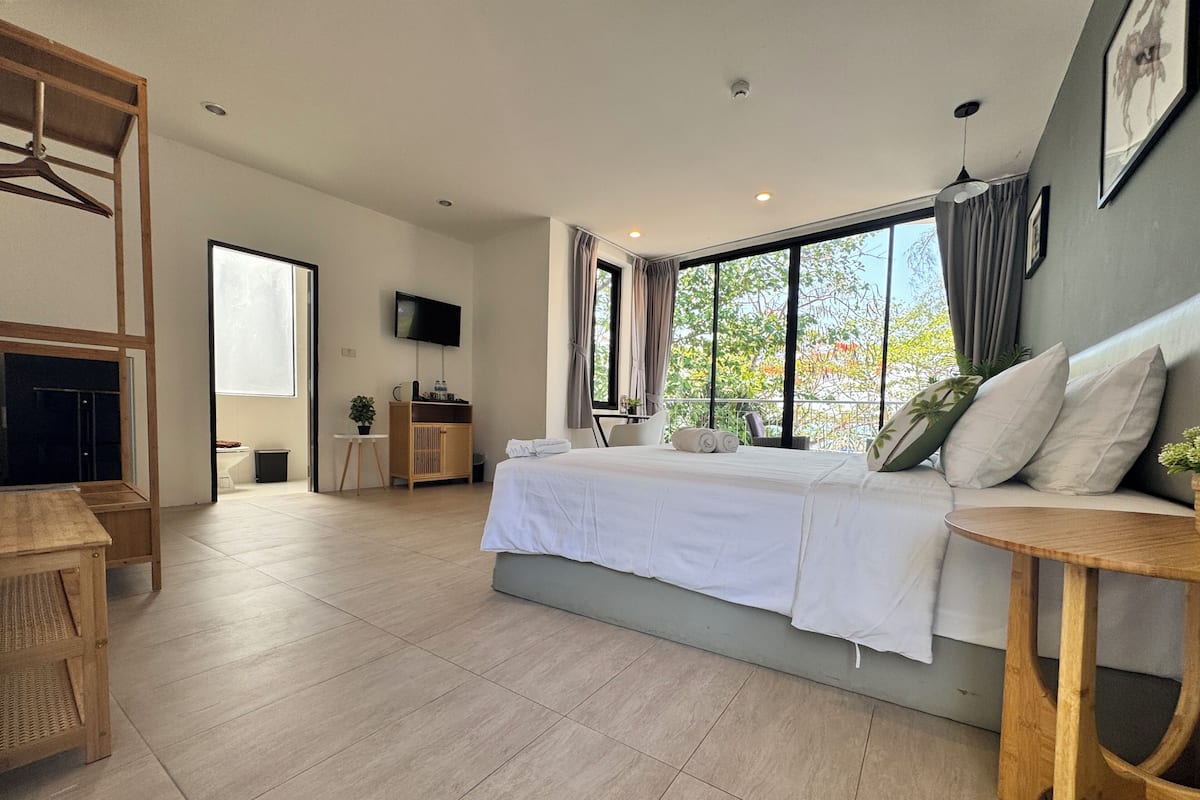 A modern hotel room with a large bed, a TV, a wooden desk, and a balcony with a view.