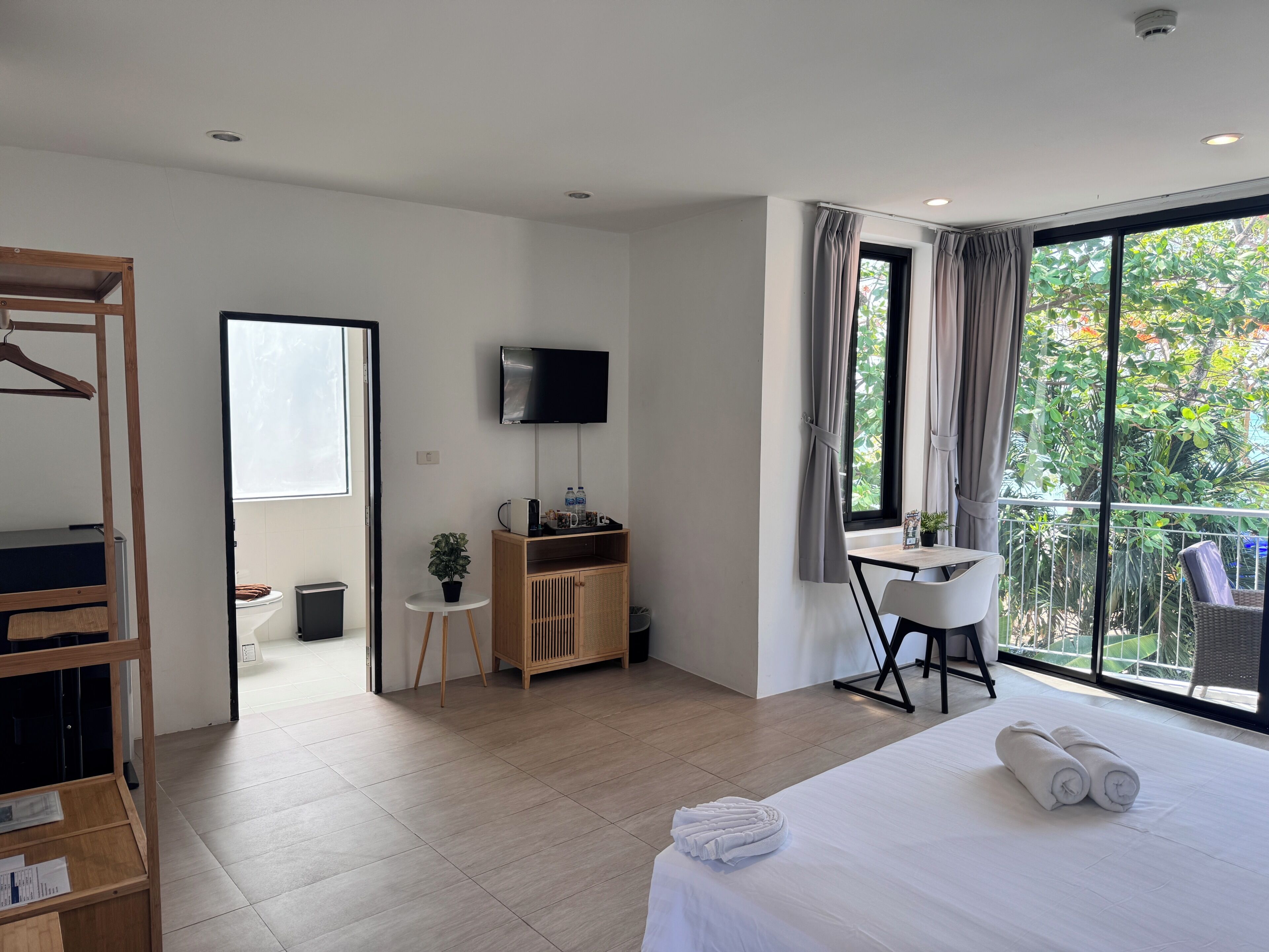 Hotelkamer met een bed, een televisie, een bureau, een stoel, een kledingkast en een balkon met uitzicht op groen.