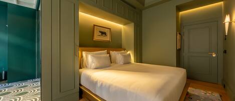 Quarto de hotel com uma cama grande, um quadro pendurado na parede e uma porta com arandela.