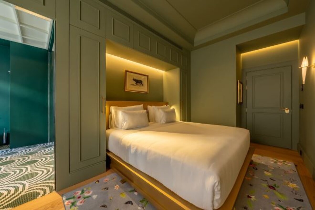 Un dormitorio con una cama grande, un cabecero con un cuadro enmarcado y una puerta con una lámpara.