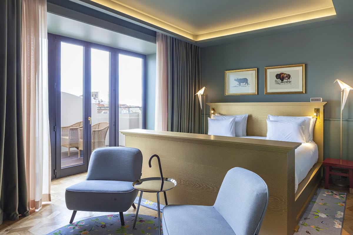 Une chambre d’hôtel avec un lit, deux chaises, une petite table, une lampe et une vue sur l’extérieur.