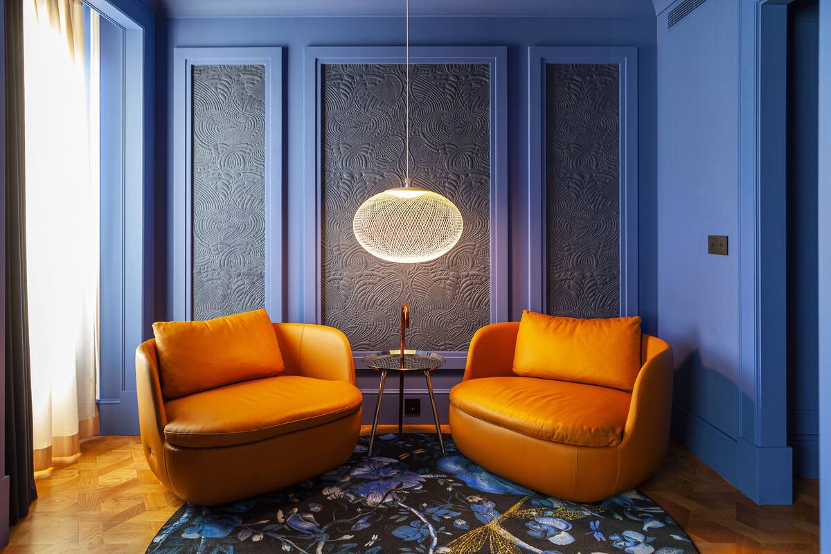 Une pièce avec deux fauteuils orange, un mur à motifs et un luminaire suspendu.