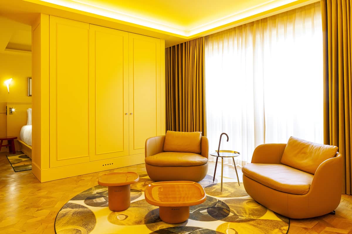 Une chambre d’hôtel moderne dotée d’une grande armoire, de deux canapés, d’une petite table et d’un tapis à motifs.