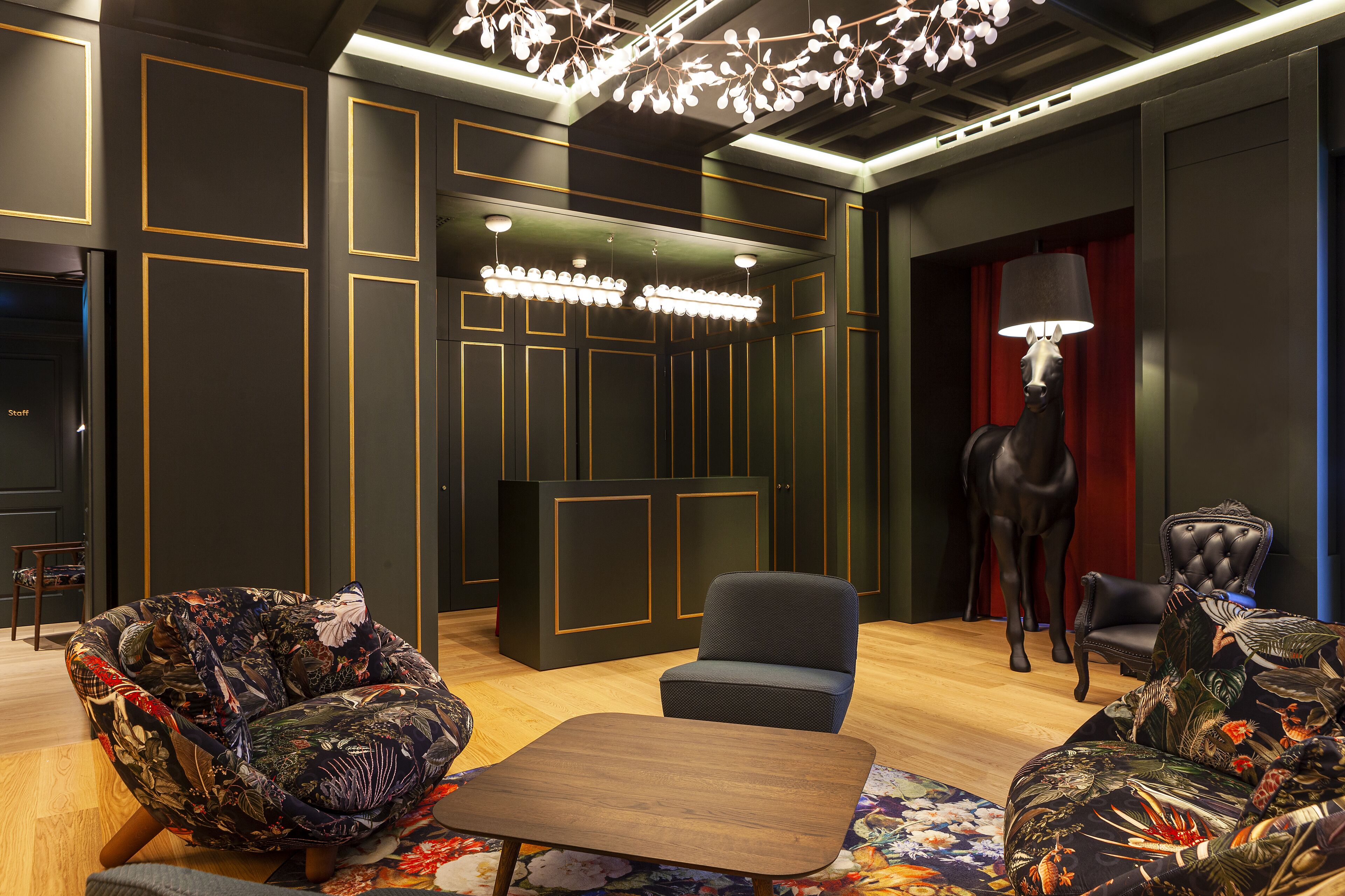 Un interior moderno con una paleta de colores oscuros, que incluye un sofá, una silla, una mesa y una estatua decorativa de un caballo.