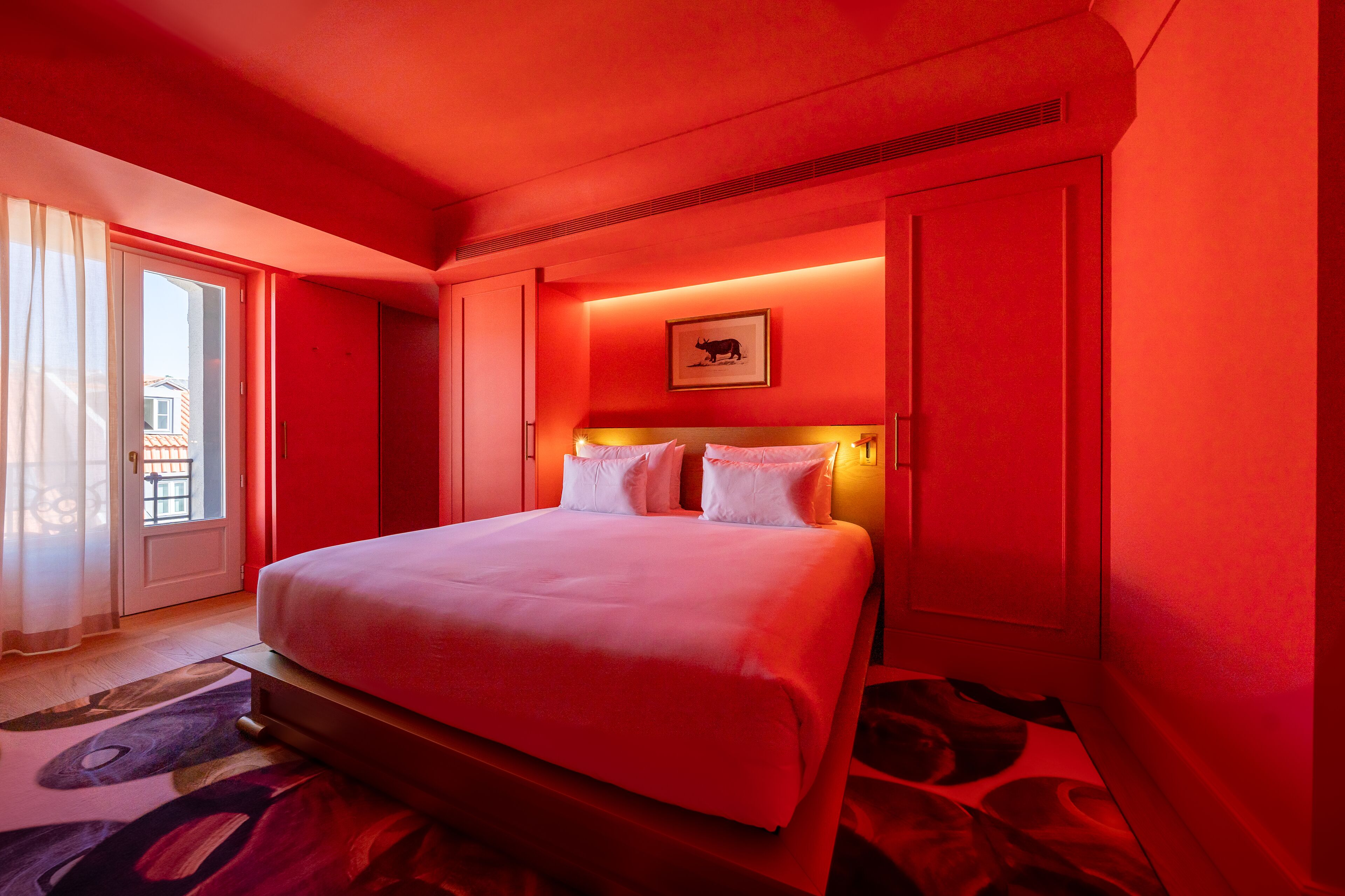 A hotel room with a large bed, a door leading to a balcony, and a framed picture on the wall.