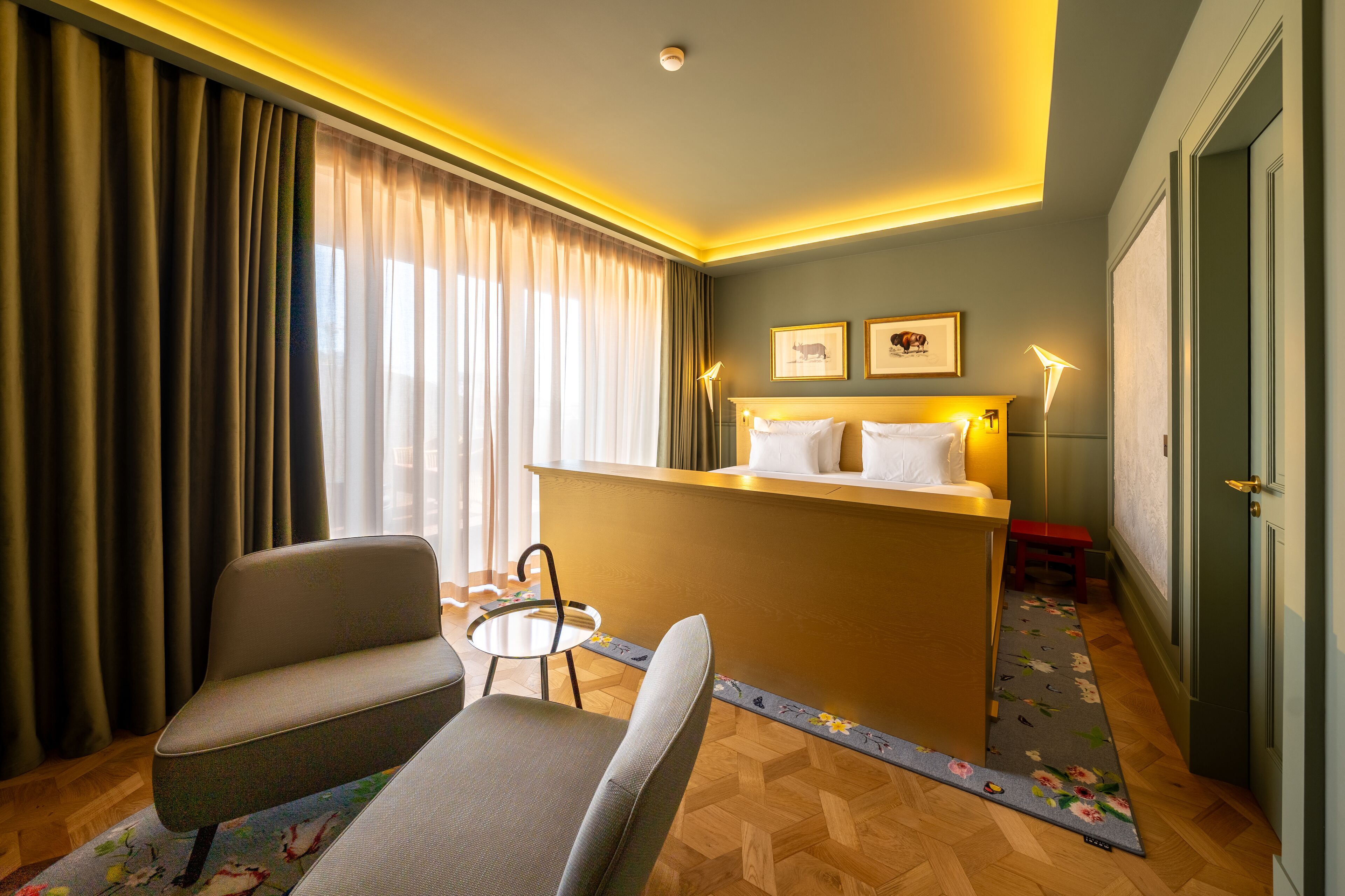 A hotel room with a bed, a desk, a chair, a small table, and a door.